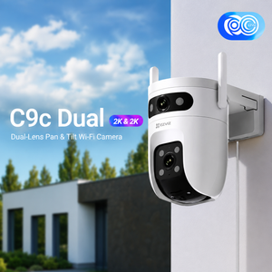 A white and black Axis C9c Dual 2K&2K pan and tilt Wi-Fi security camera mounted on a white exterior wall, with a blurred house and blue sky in the background and an Axis logo badge in the top right.